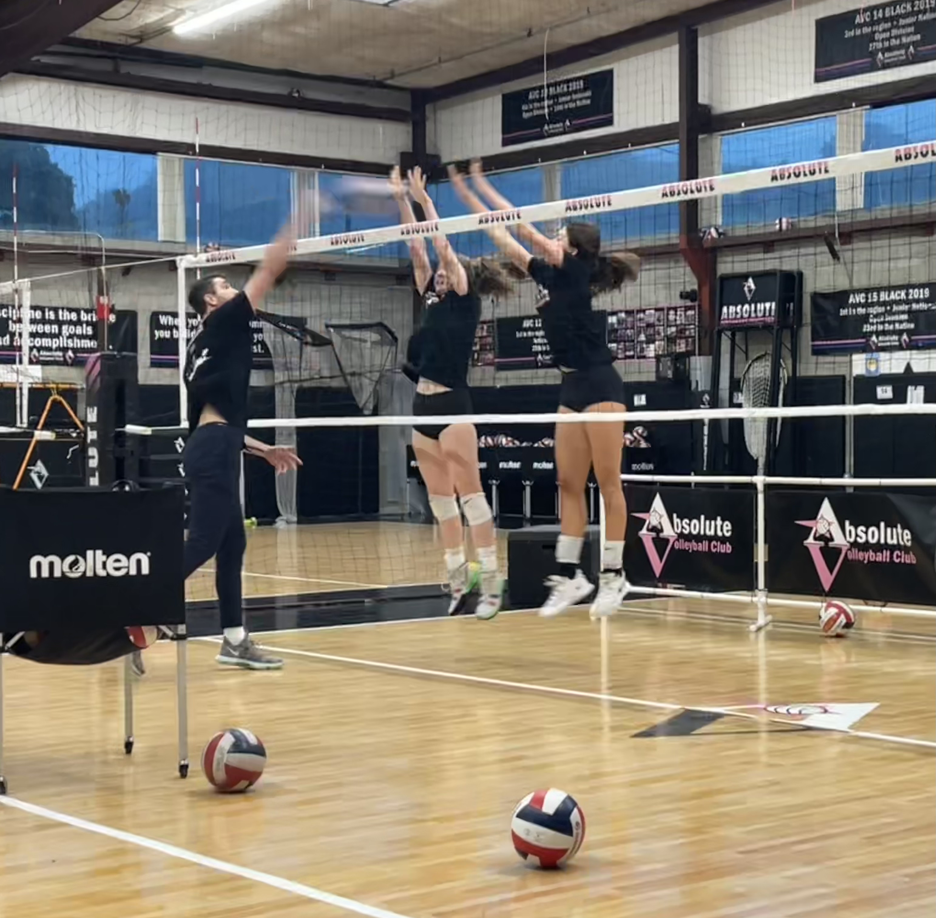 Shows a trainer working with two volleyball players on blocking at the next